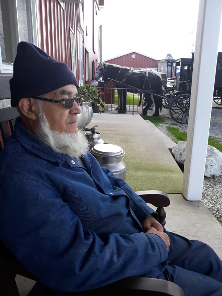 Amish man on farm porch with horse and buggies.