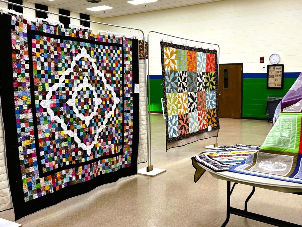 2 quilts hanging and one on chair