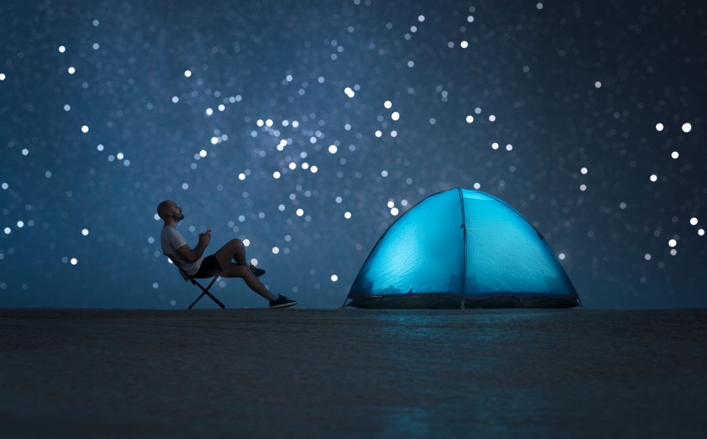 A man relaxing in a chair outdoors with a tent and starry sky.