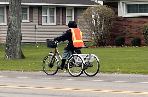 A woman rides an adult trike in Shipshewana while wearing a safety vest.