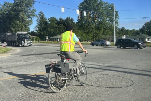 A man rides a regular bicycle while wearing a safety vest. 